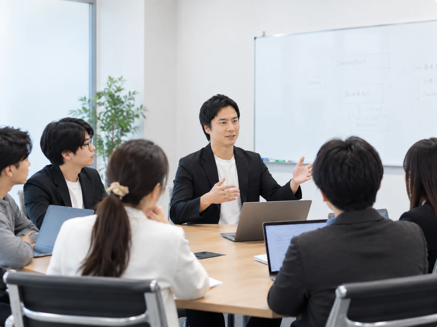ホワイトボードを前に、黒宮代表がチームと意見を交わすイメージ